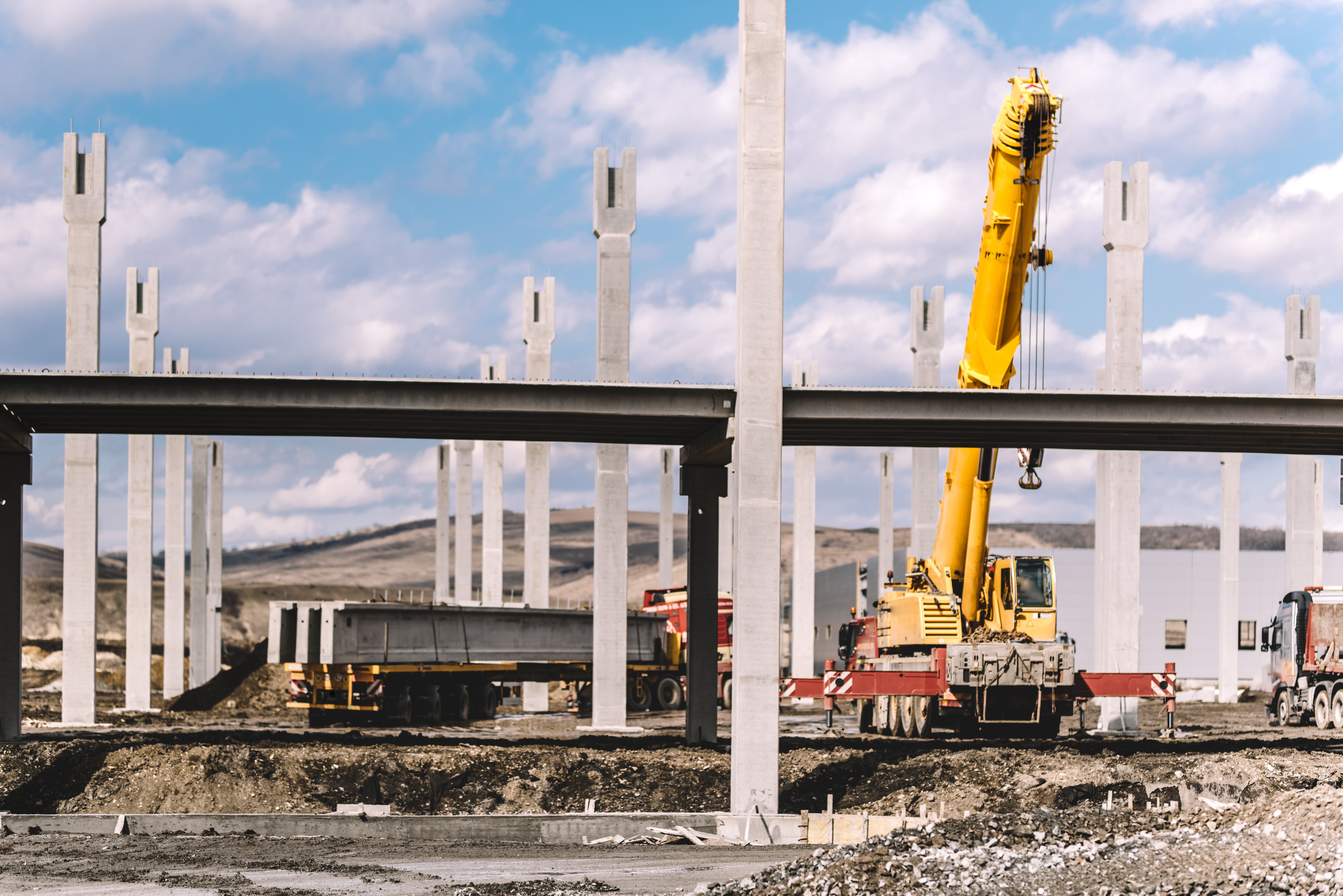 Industrial construction site with prefabricated concrete pillars, heavy duty crane, cargo and trucks